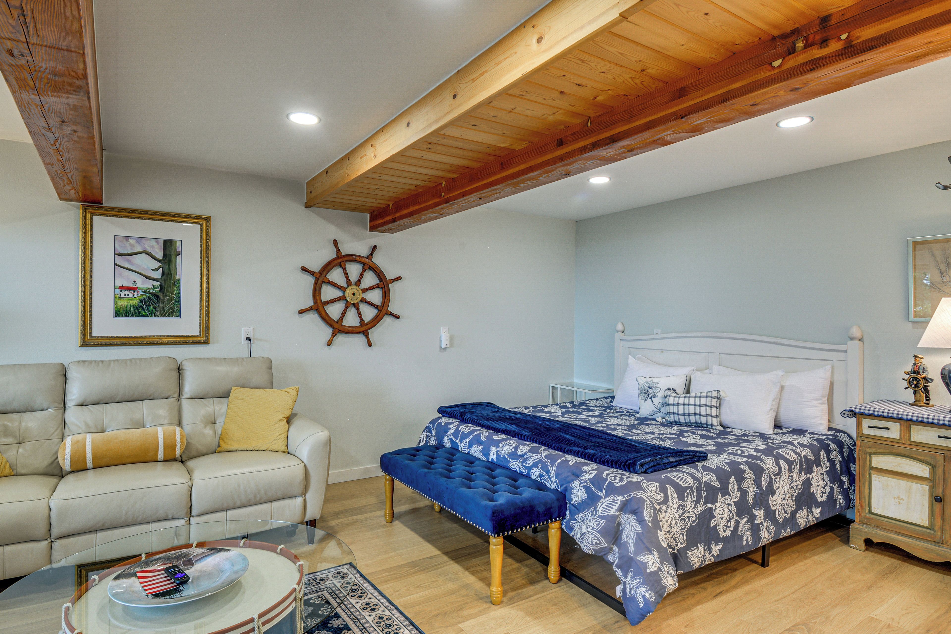 A room with a bed, a sofa, a wooden ceiling, and a wall-mounted ship's wheel.