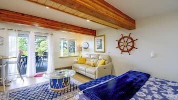 A living room with a wooden ceiling, a white sofa with yellow cushions, a blue patterned rug, and a ship's wheel decoration.