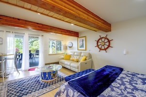 Uma sala de estar com teto de madeira, um sofá branco com almofadas amarelas, um tapete azul estampado e uma decoração com o volante de um navio.