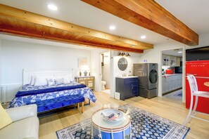 A bedroom with a bed, bedside table, lamp, and a view into the adjacent kitchen. - Puget Sound Views & Patio: Point No Point Apt (Hansville)