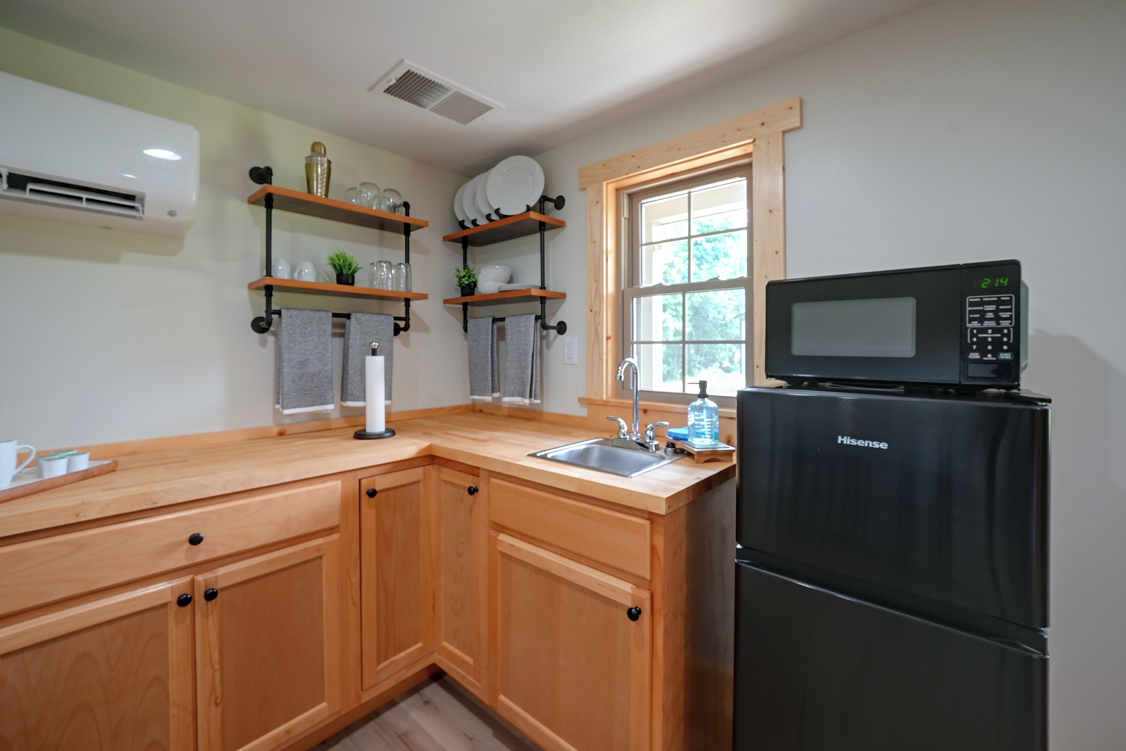 Una cocina con armarios de madera, un refrigerador negro, un microondas y una ventana con vistas a árboles.