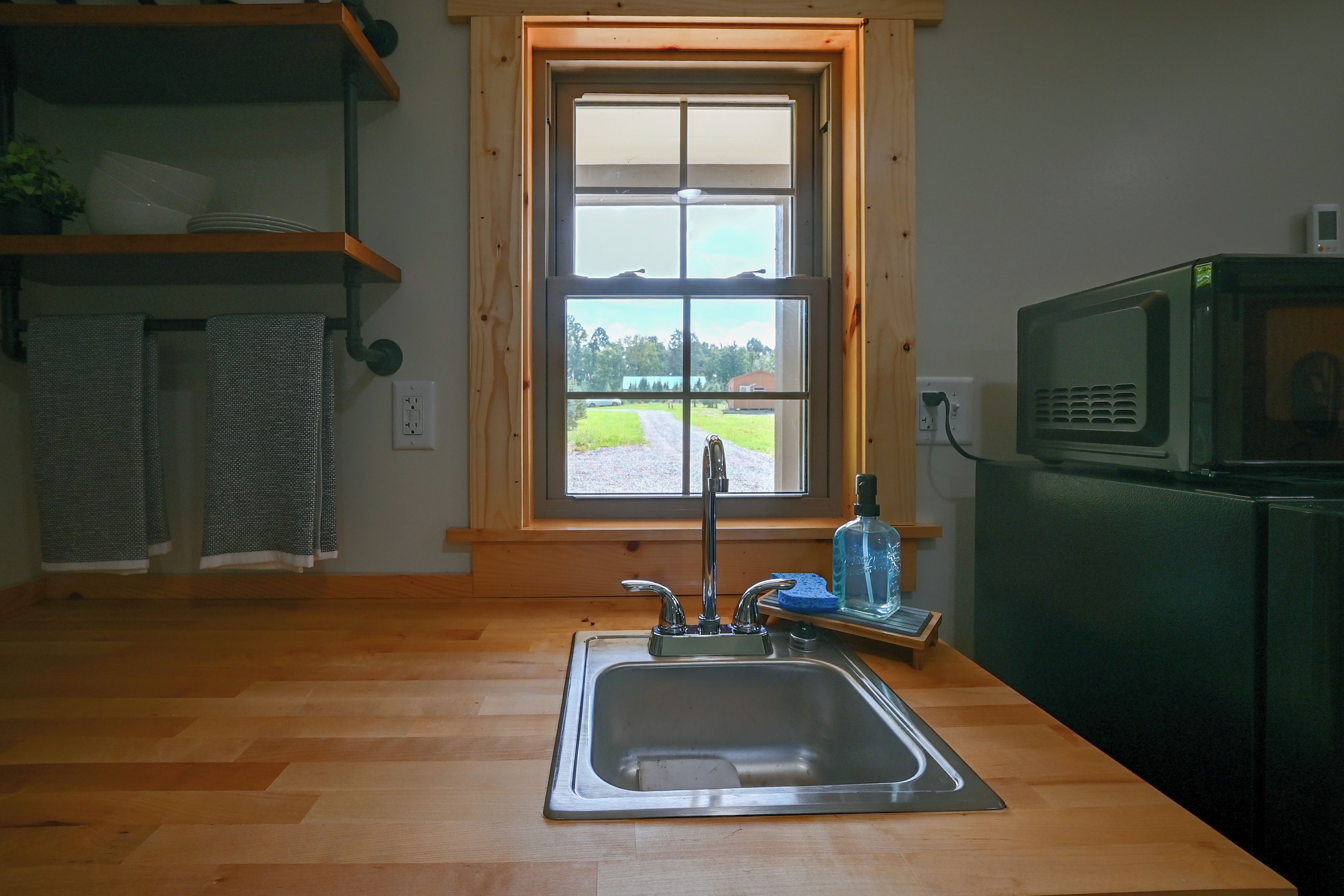 Una cocina con encimera de madera, un lavamanos de acero inoxidable, una ventana con vistas al exterior y un microondas.