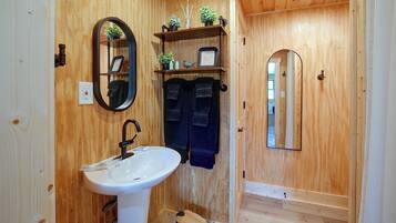 Un baño con paneles de madera, un lavamanos blanco, un espejo y un perchero para toallas.
