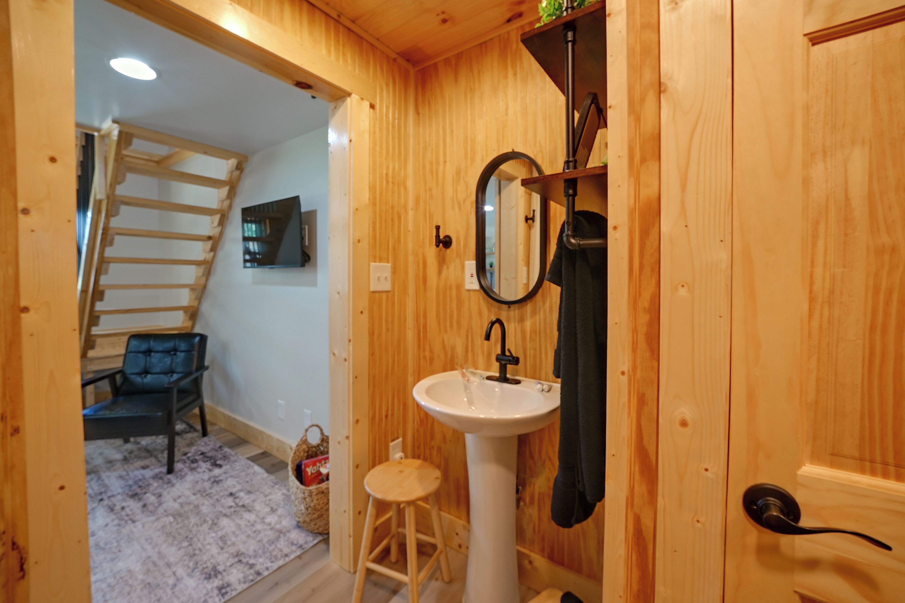 Un interior de madera con un lavabo blanco, un espejo, una toalla, un taburete y una silla.