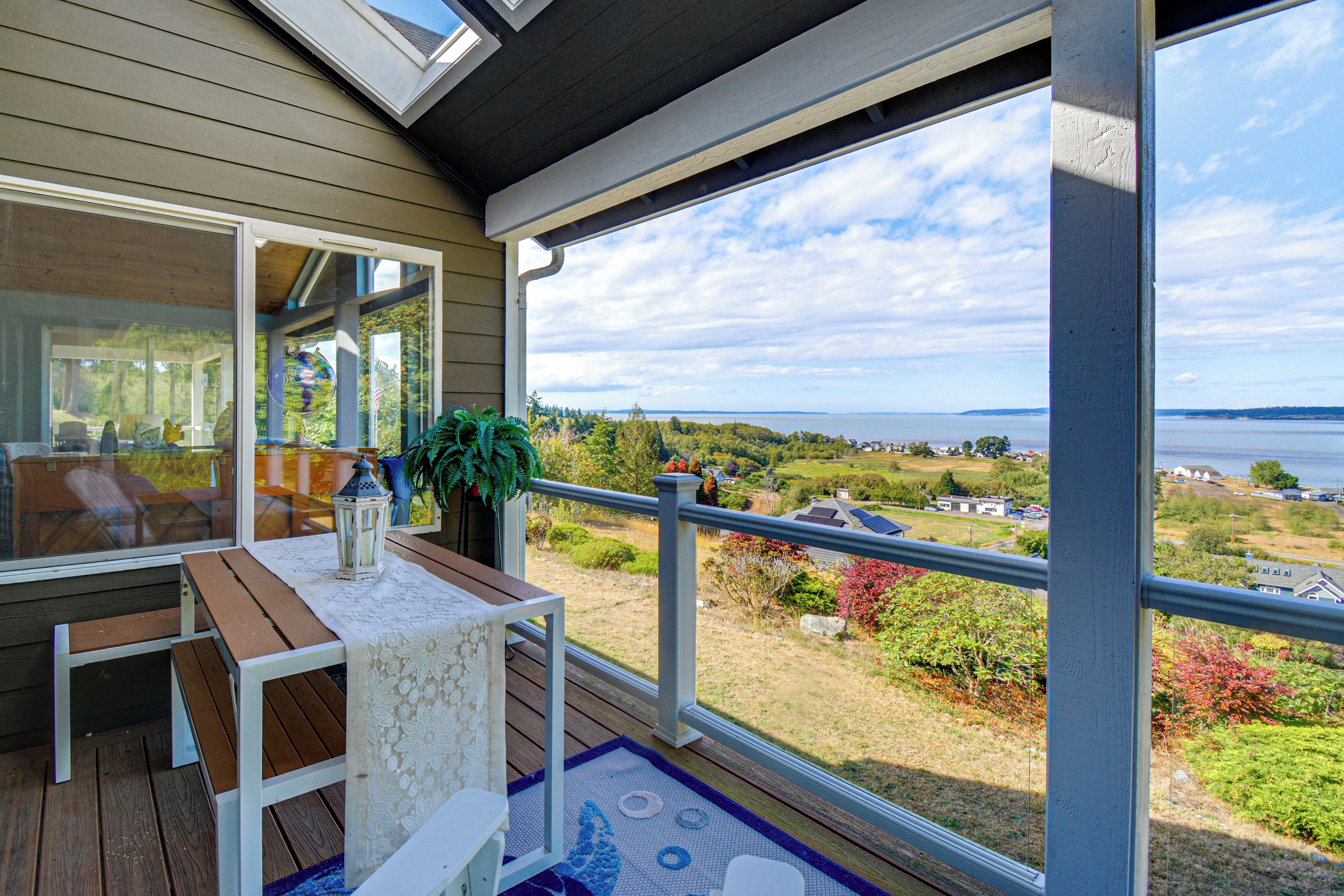 A balcony with a table, chairs, and a view of a landscape with trees and a body of water.