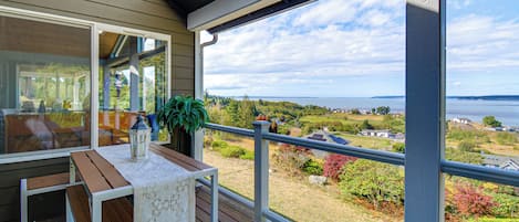 A balcony with a table, chairs, and a view of a landscape with trees and a body of water.