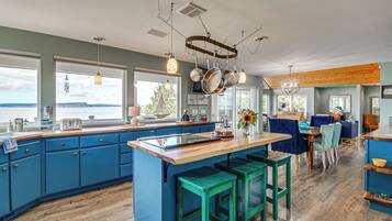 A modern kitchen with blue cabinets, a wooden island, and a view of the water.
