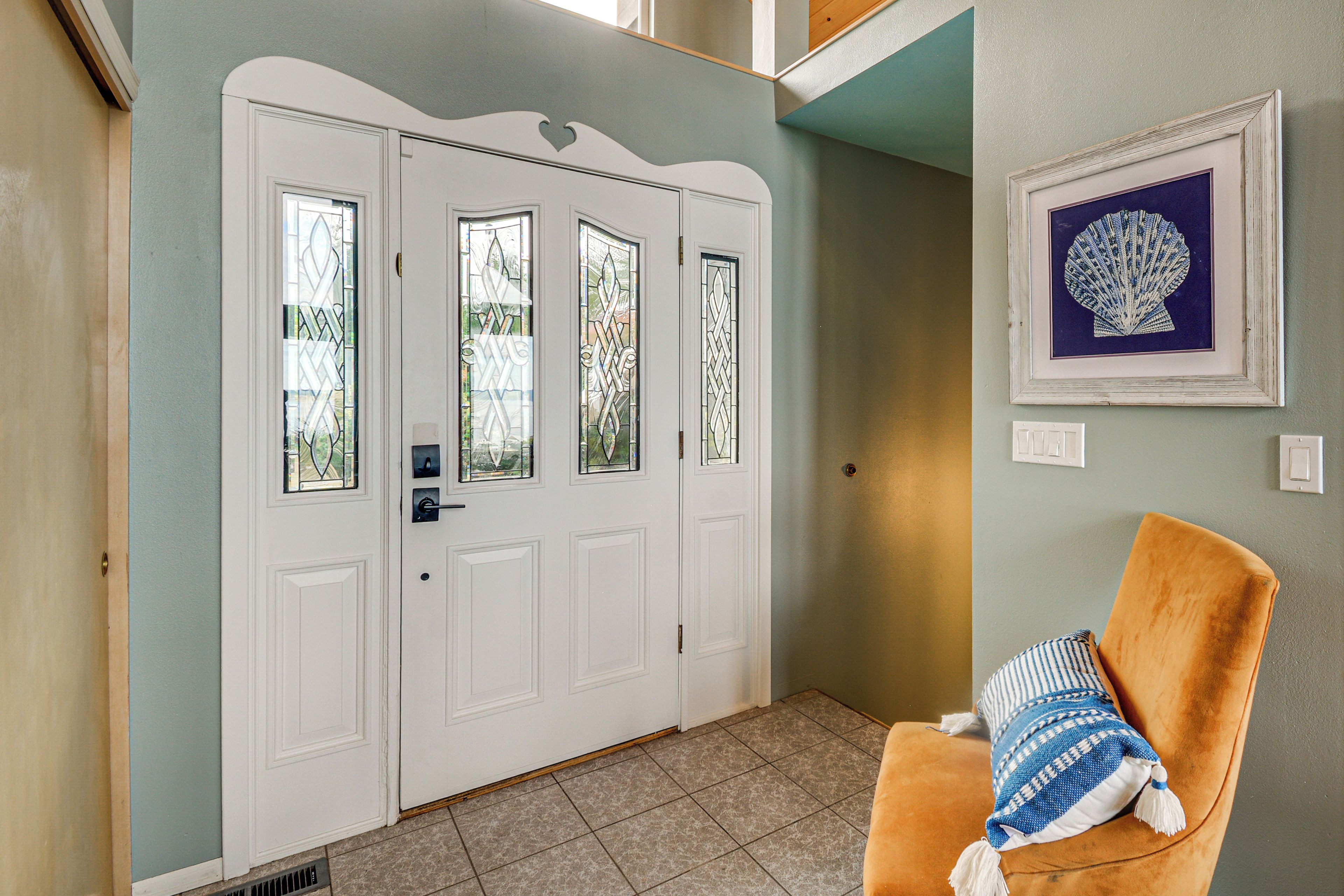 A closed white door with a window, a framed picture on the wall, and a brown chair with a striped pillow.