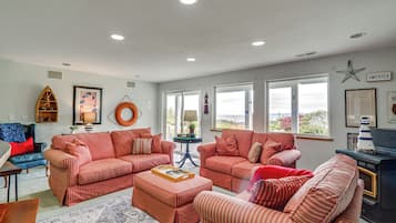 A living room with two red-striped sofas, a coffee table, and a wooden side table. There are two windows with a view of the outdoors.