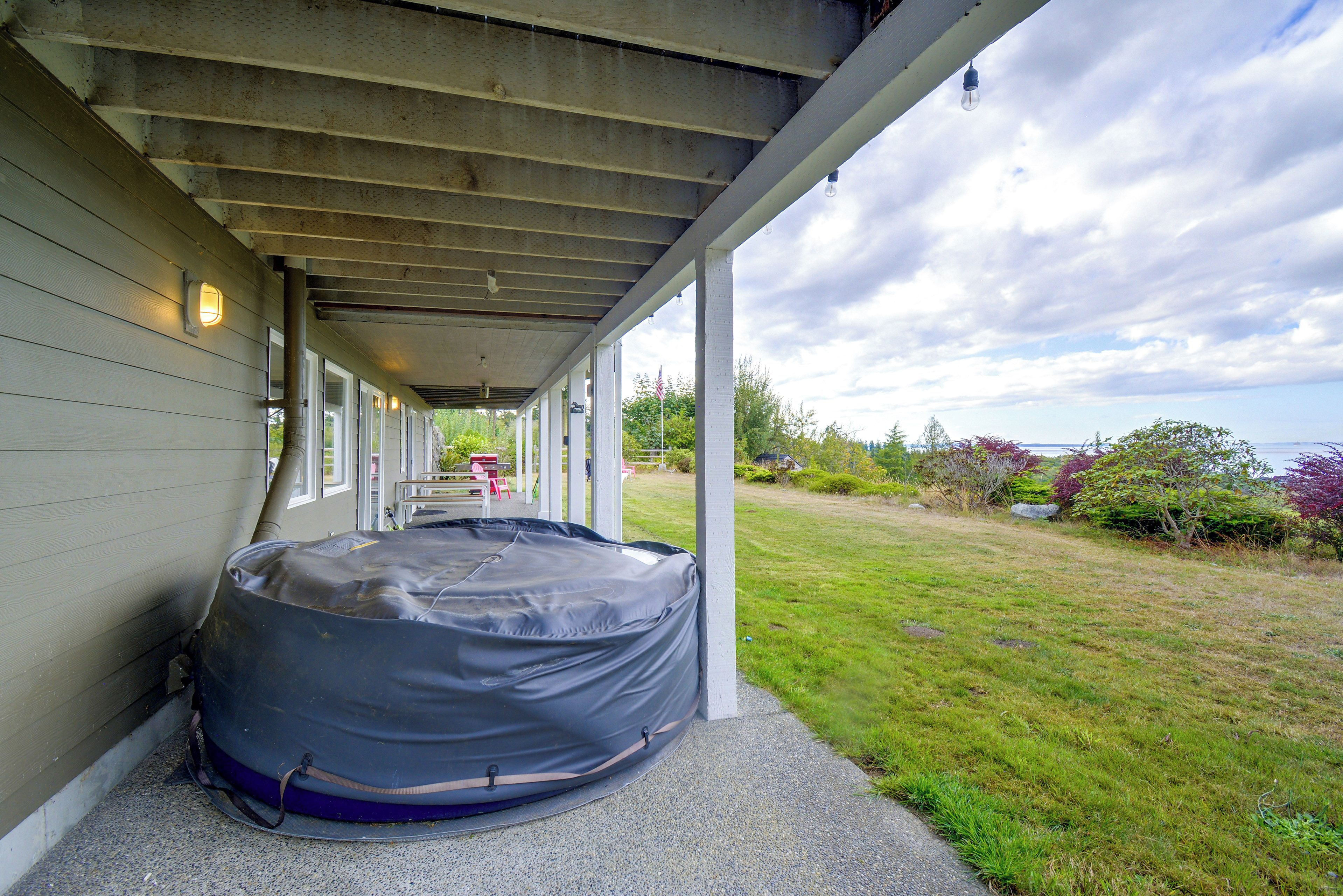 A covered outdoor area with a hot tub, a concrete floor, and a grassy yard.