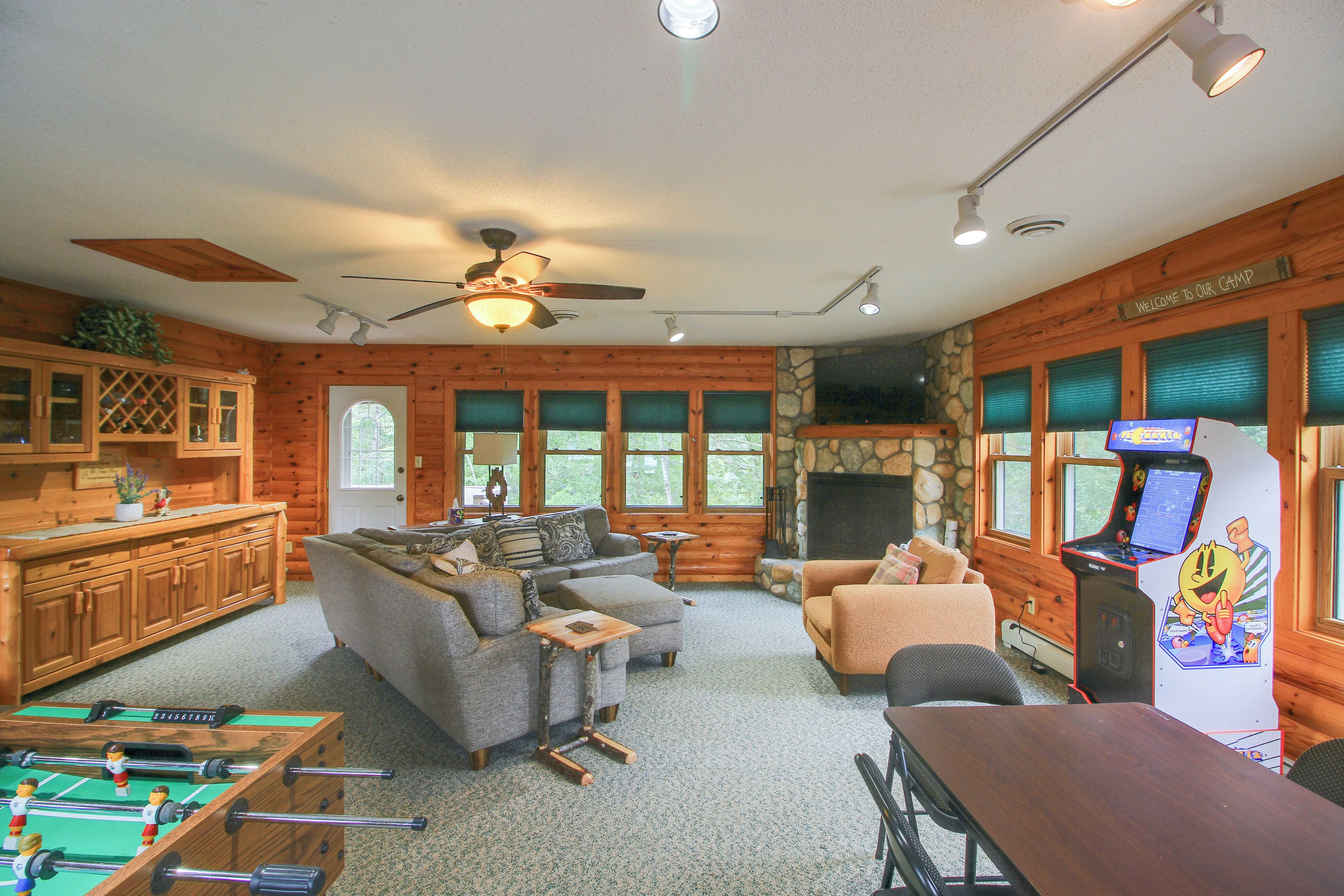 A cozy cabin interior with a fireplace, wooden furniture, a foosball table, and a Nintendo gaming console.
