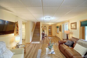 A living room with a brown leather sofa, a glass coffee table, a television mounted on the wall, and a staircase leading to another level. - Sibley Shores Lake Cabin w/ Dock & Deck! (Pequot Lakes)
