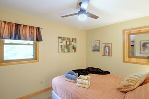 Ein Schlafzimmer mit Bett, Deckenventilator, Fenster mit Vorhängen und Wandbildern.