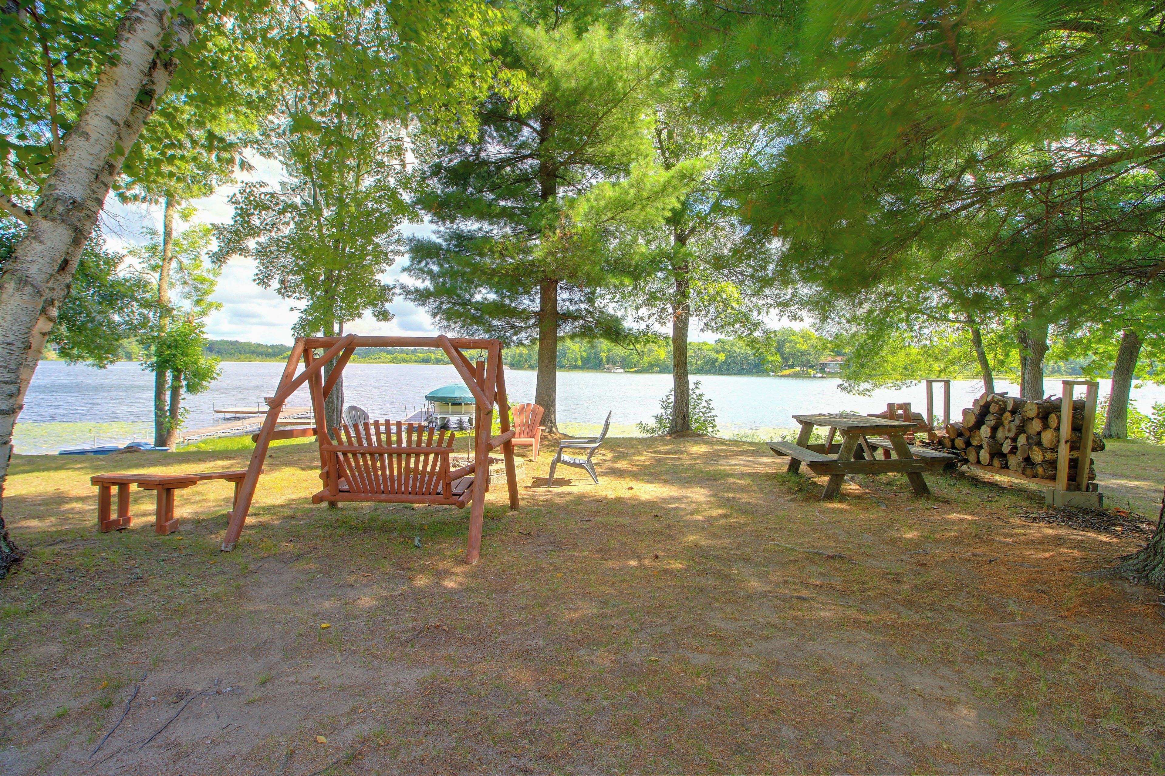 Un camping junto al lago con un conjunto de columpios, una mesa de picnic y bancos.