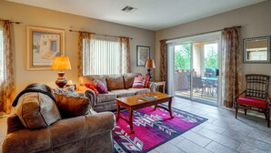 A living room with a sofa, a coffee table, and a chair. There is a window with curtains, a door leading to an outdoor area, and a wall with a framed picture. - Desert-view Green Valley Retreat Near Golf Courses (Green Valley)