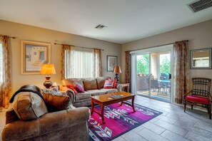 A living room with a sofa, a coffee table, and a chair. There is a window with curtains, a door leading to an outdoor area, and a wall with a framed picture. - Desert-view Green Valley Retreat Near Golf Courses (Green Valley)