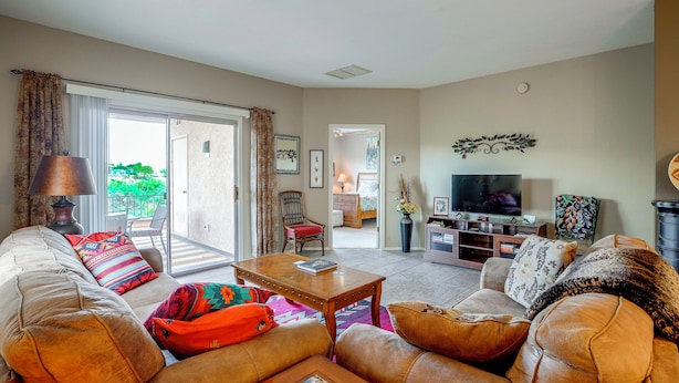 A living room with a sofa, armchair, coffee table, and a television. There is a sliding glass door leading to a balcony. - Desert-view Green Valley Retreat Near Golf Courses (Green Valley)