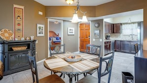 A dining area with a wooden table, chairs, and a chandelier. There is a kitchen visible in the background with dark cabinets and a window. - Desert-view Green Valley Retreat Near Golf Courses (Green Valley)