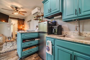 Une cuisine avec des meubles de couleur turquoise, un réfrigérateur en acier inoxydable, une machine à café et un ventilateur de plafond.