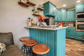 Une cuisine avec des meubles de couleur turquoise, un îlot central, des tabourets et une machine à café.