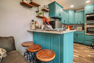 A kitchen with teal cabinets, a central island, stools, and a coffee machine.