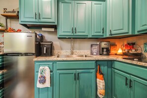 Una cocina con gabinetes verde azulado, electrodomésticos de acero inoxidable y una cafetera.