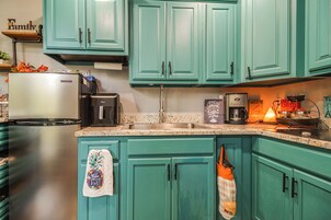Una cocina con gabinetes verde azulado, electrodomésticos de acero inoxidable y una cafetera.