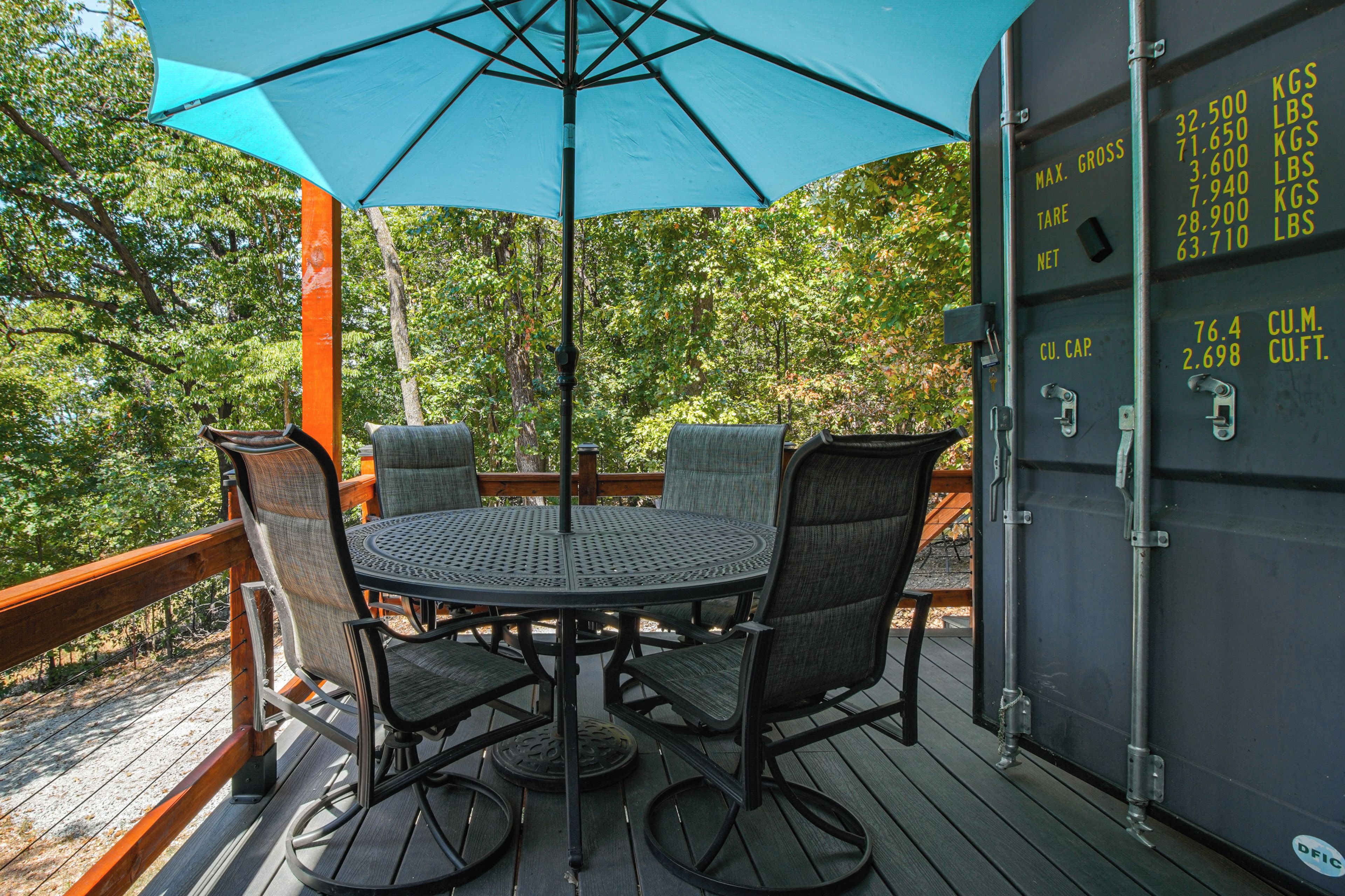 An outdoor patio with a round table and chairs, a blue umbrella, and a wooden deck.