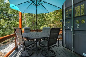 An outdoor patio with a round table and chairs, a blue umbrella, and a wooden deck.