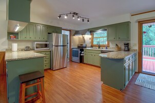 Una cocina con armarios verdes, un refrigerador de acero inoxidable, un microondas y una cafetera.