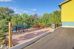 An outdoor seating area with picnic tables and benches, surrounded by trees and a building.