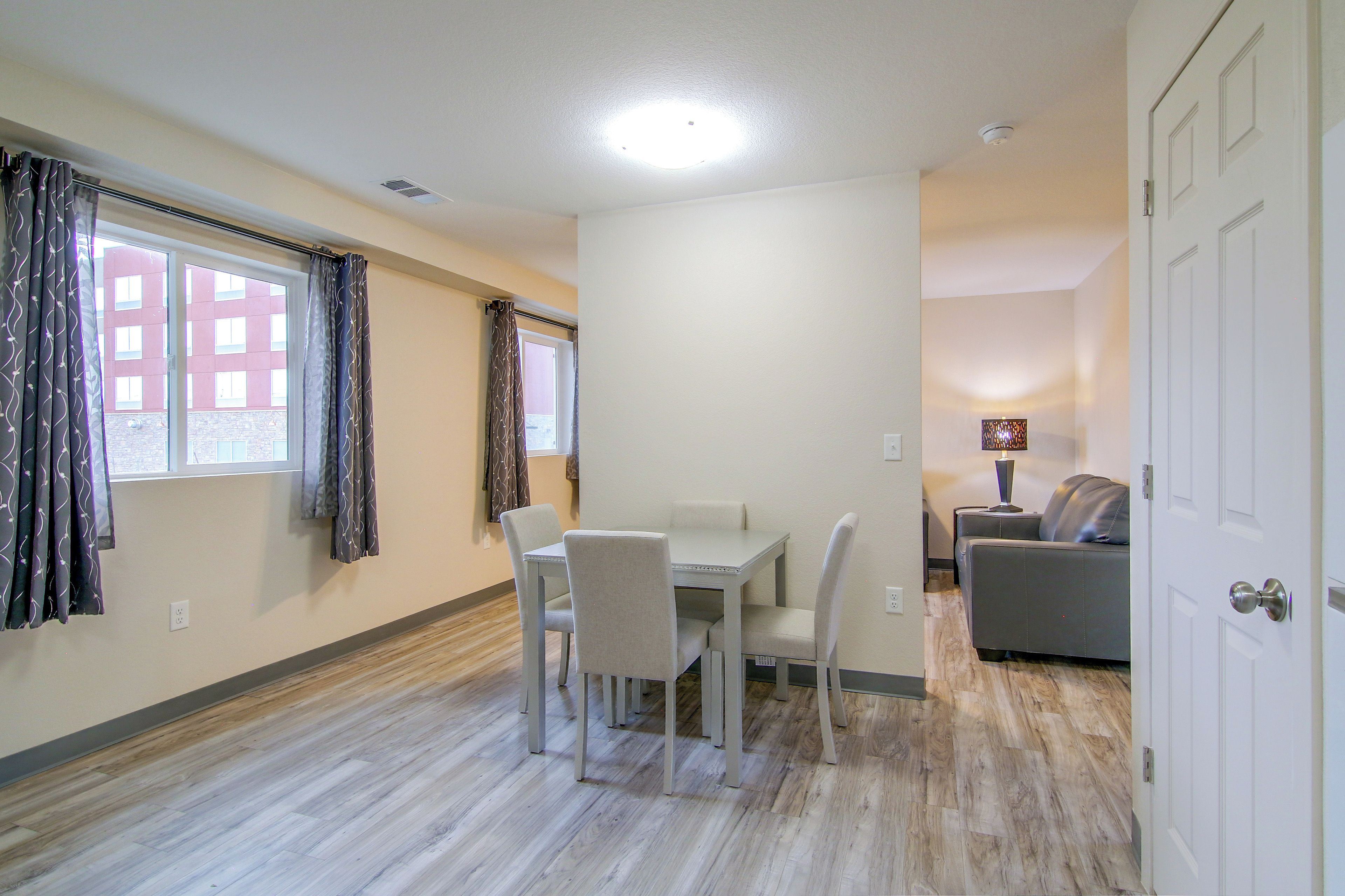 A room with a dining table, chairs, a sofa, and a lamp.