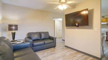 A living room with a sectional sofa, a flat-screen TV mounted on the wall, and a ceiling fan.