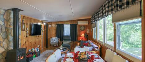 A cozy cabin interior with a dining table set for four, a fireplace, and a television mounted on the wall.