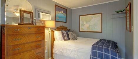 A bedroom with a wooden dresser, a bed with a blue blanket, a map on the wall, and a lamp.