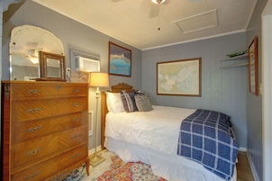 A bedroom with a wooden dresser, a bed with a blue blanket, a map on the wall, and a lamp.