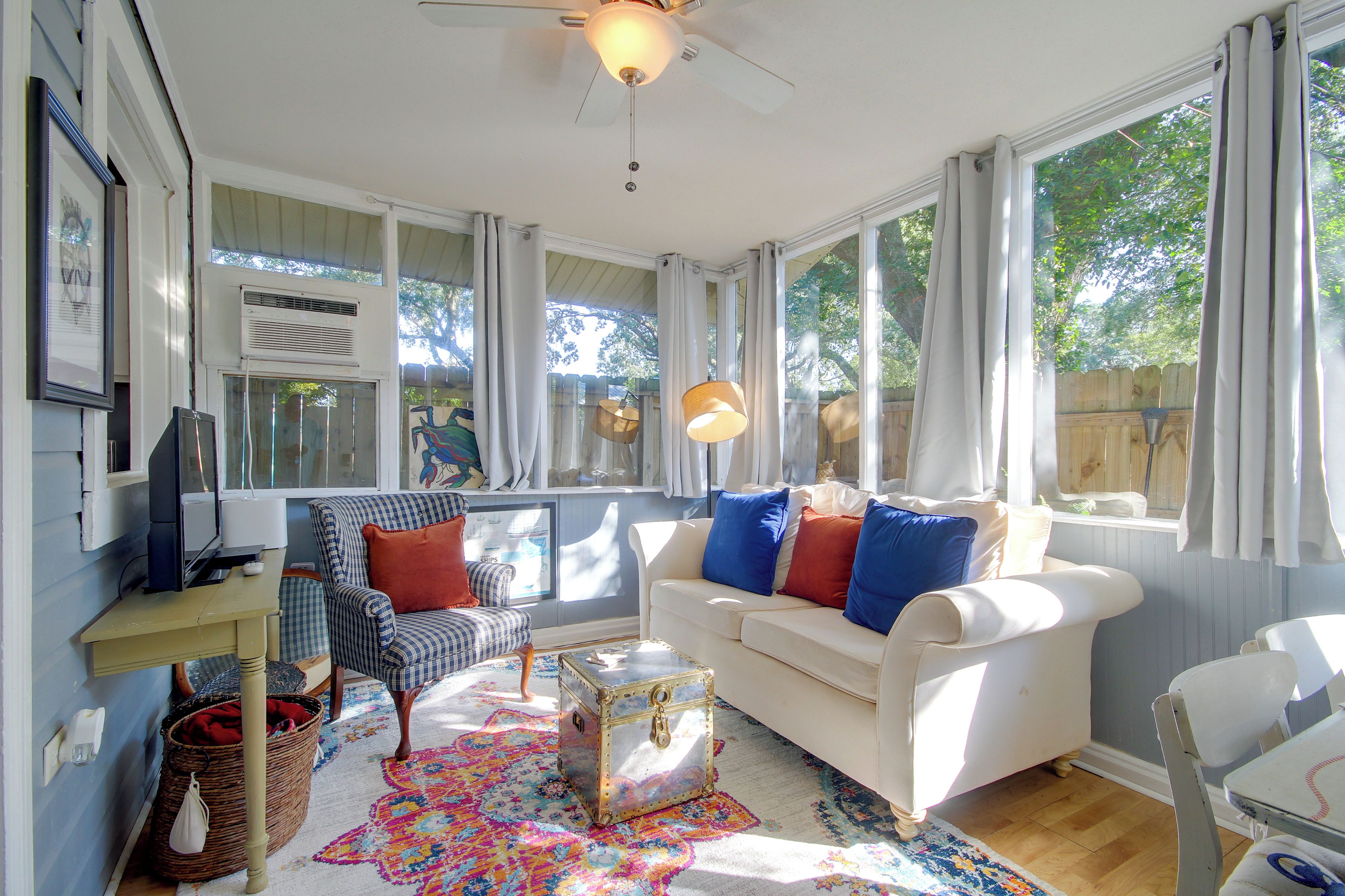 A room with a white sofa, a patterned rug, a wicker basket, and a ceiling fan.