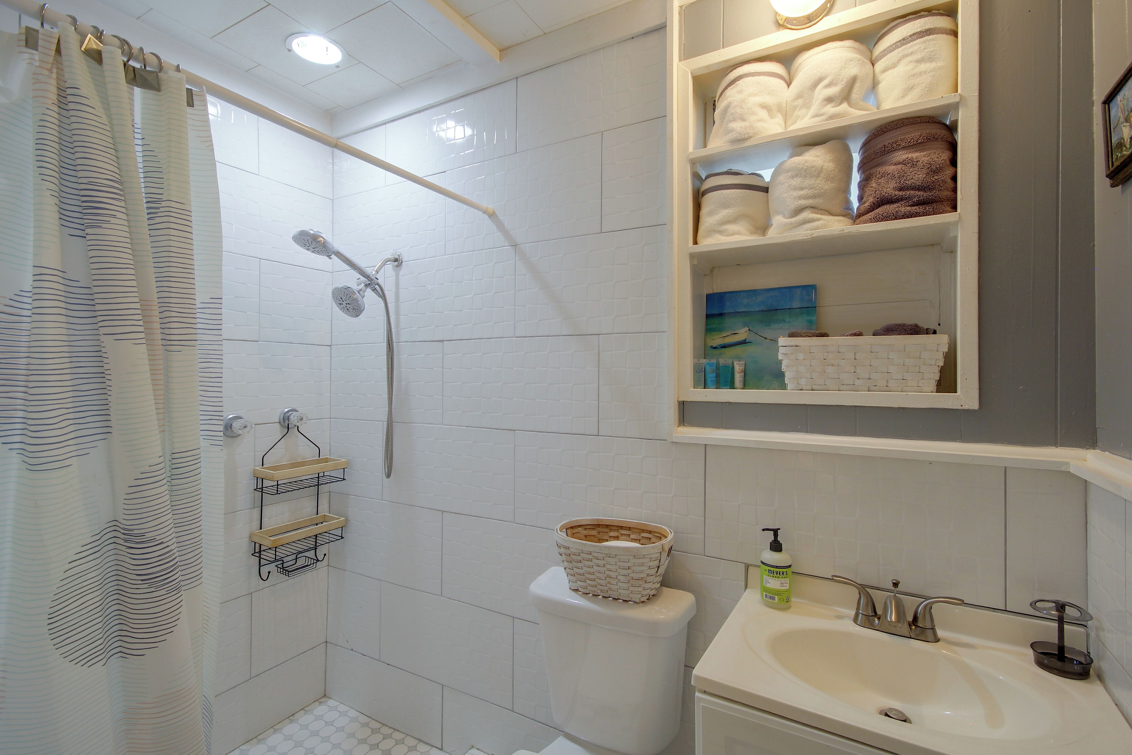 A bathroom with a shower, toilet, sink, and towel storage.