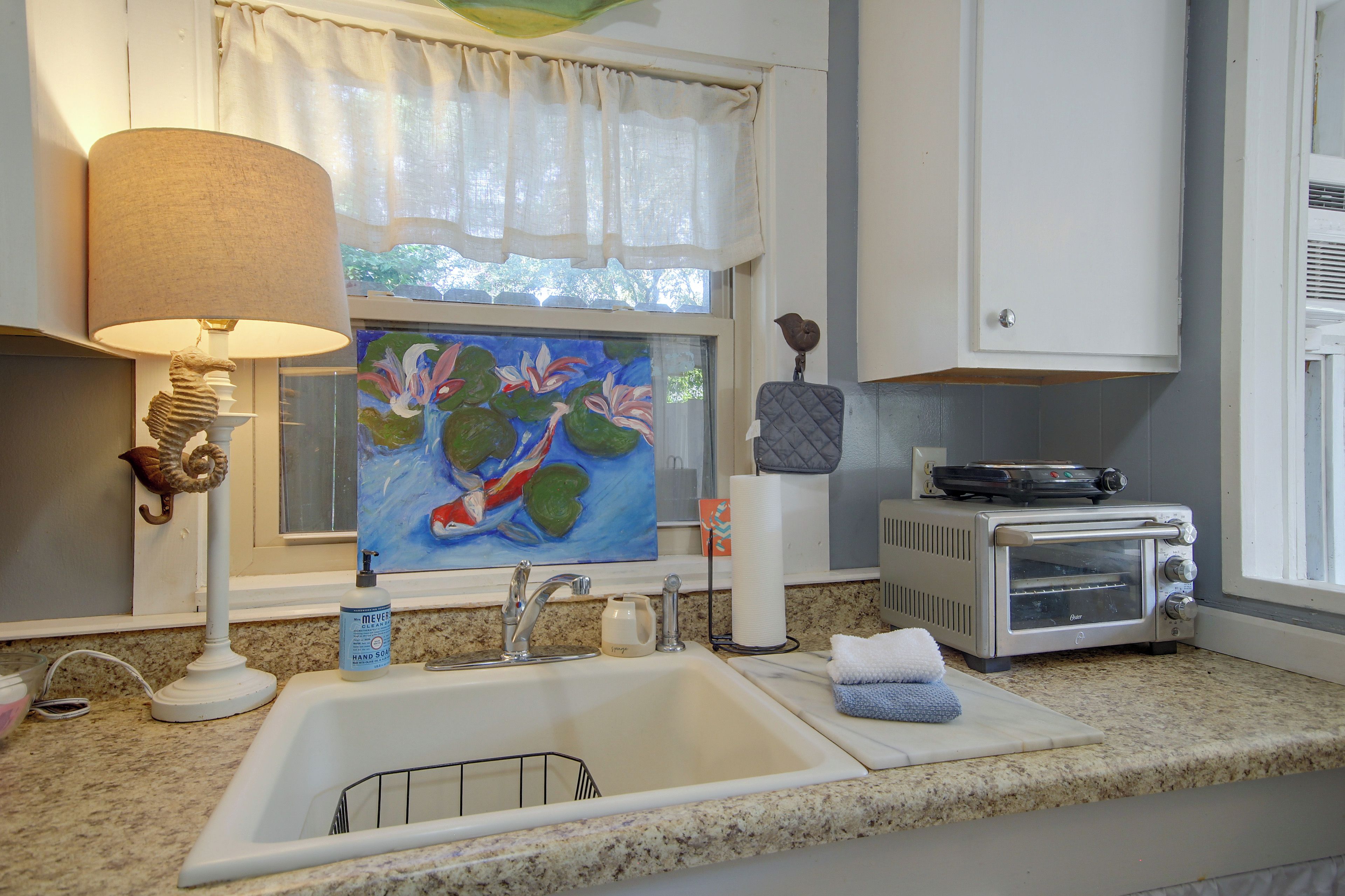 A kitchen with a sink, a toaster, a painting, a lamp, and a decorative seahorse.