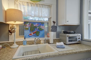 Una cocina con un lavamanos, un tostador, un cuadro, una lámpara y un caballito de mar decorativo.