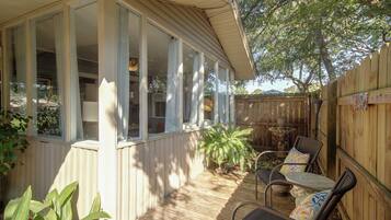 Un patio cubierto con terraza de madera, zona de estar con sillas y una mesa, y vista al patio trasero.