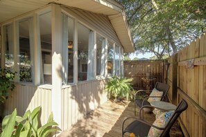 Ein überdachter Patio-Bereich mit Holzboden, eine Sitzecke mit Stühlen und Tisch, und Blick zum Garten.