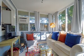 Ein Wohnzimmer mit einer Couch, einem Sessel, einem Fernseher und einem Fenster mit Vorhängen.