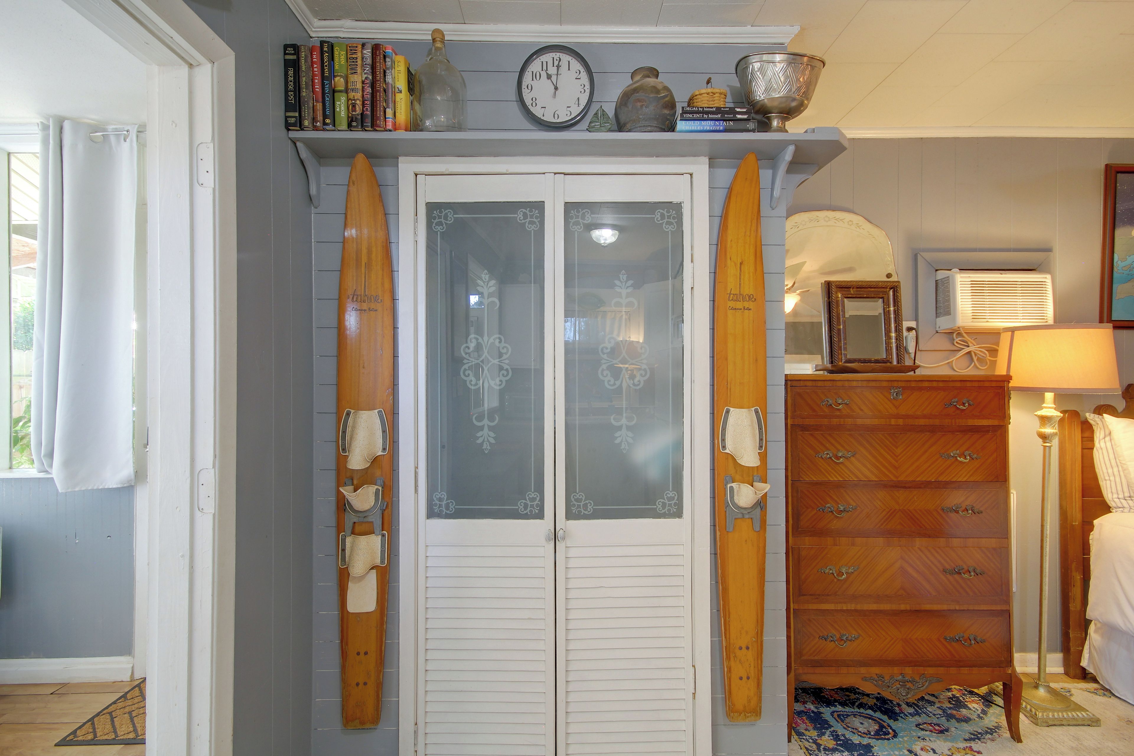 A room with a wooden door, a clock, a shelf with books, and a surfboard.