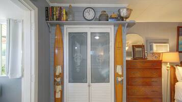 A room with a wooden door, a clock, a shelf with books, and a surfboard.