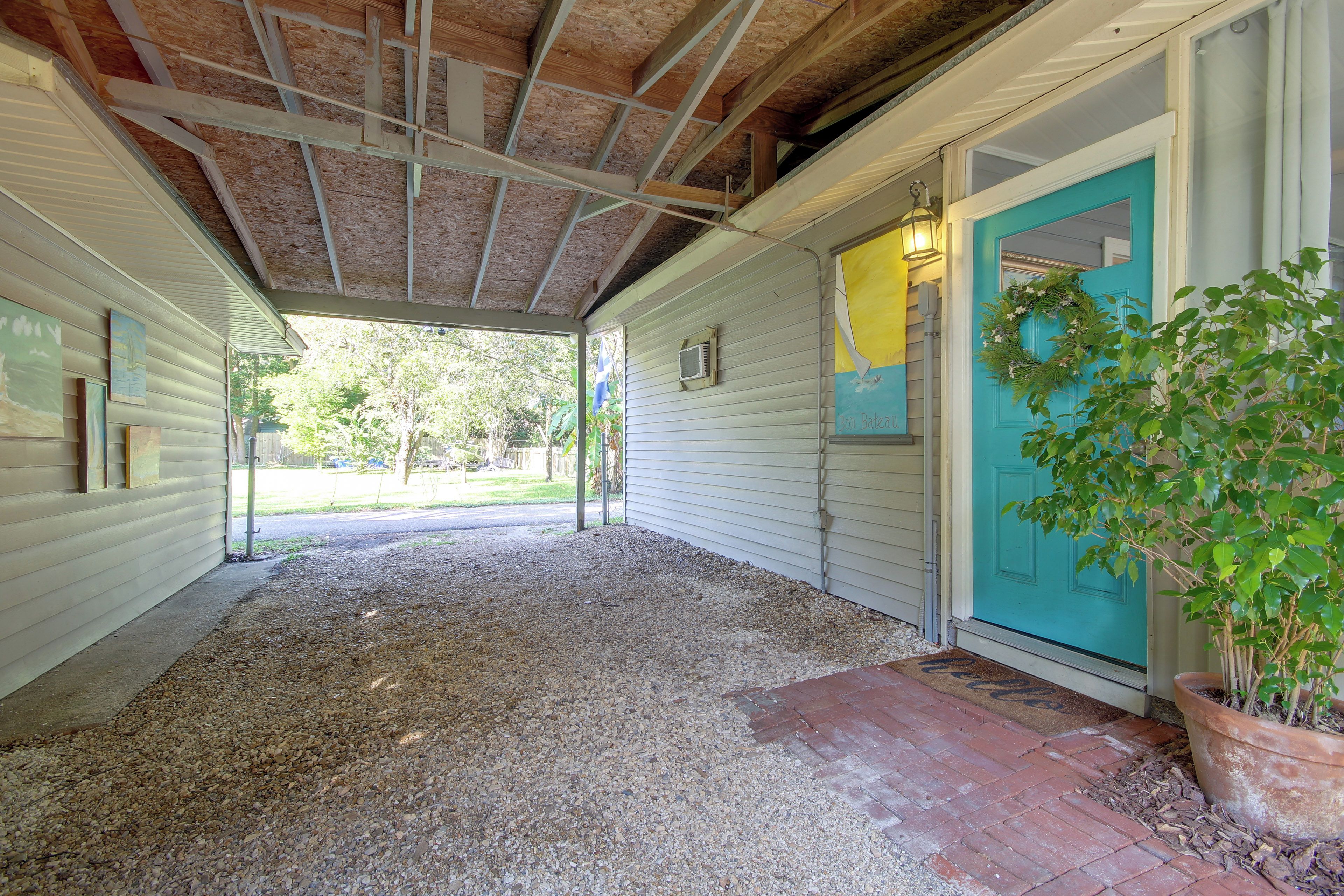 A covered porch with a gravel floor, a door with a wreath, and a potted plant.