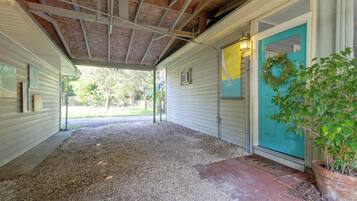 A covered porch with a gravel floor, a door with a wreath, and a potted plant.