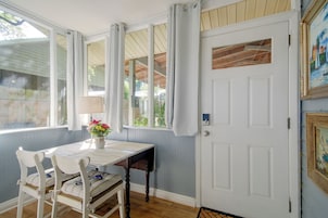 A room with a white door, a table with chairs, a vase with flowers, and a window with curtains.