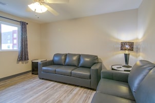 A modern living room with a leather sofa, a side table with a lamp, a ceiling fan, and a window with curtains.