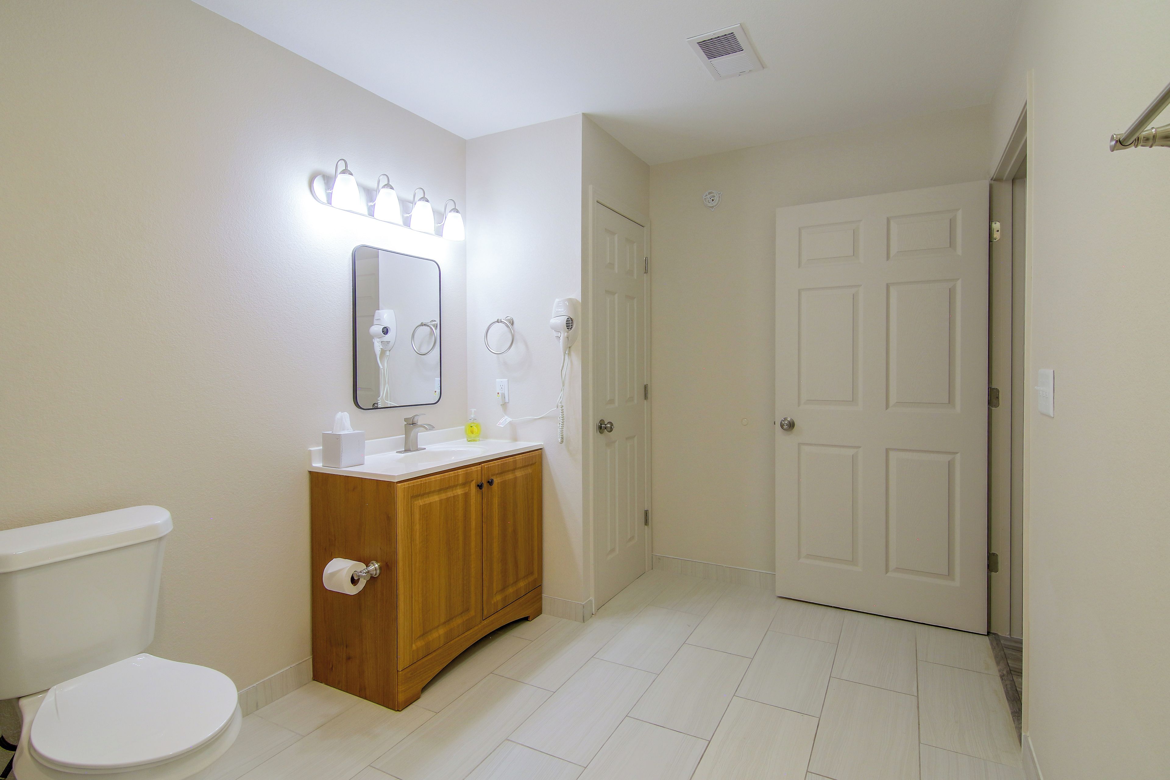 A bathroom with a toilet, vanity, mirror, and a door leading to another room.